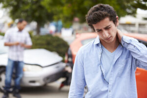 Car Accident Lawyer Bergen County, NJ with a man holding his neck in pain standing in front of a recent car accident